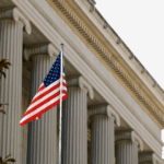 American flag flying in front of a neoclassical government building with tall stone columns, symbolizing public service, governance, and institutional leadership.
